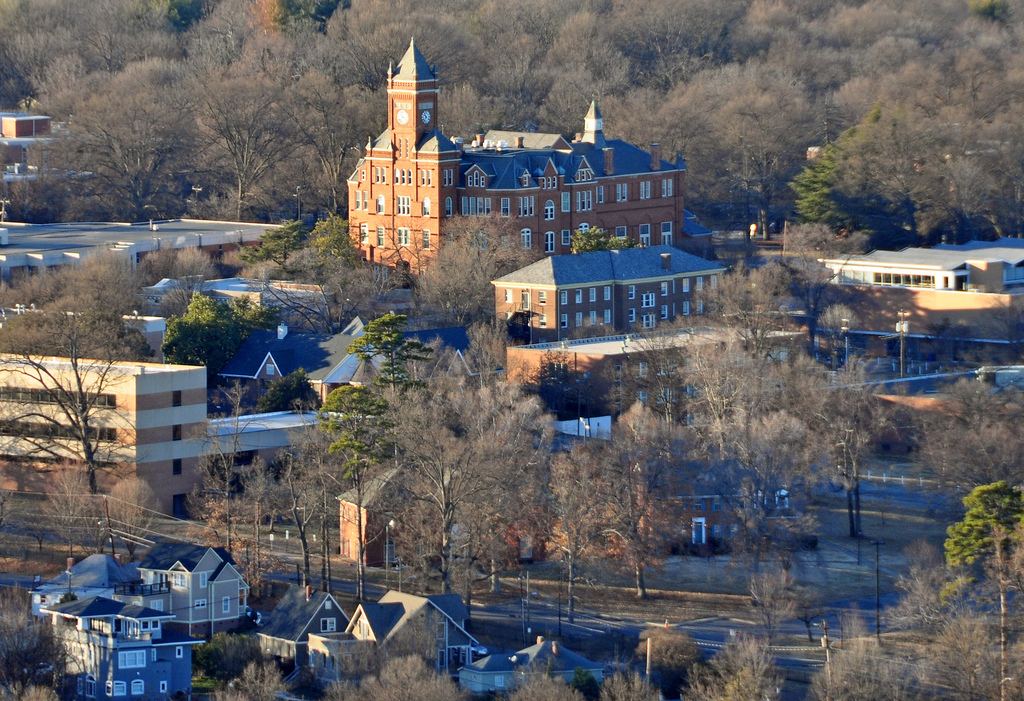 Elevated view across a hillside campus of bare winter trees, with a red brick building topped by a tall clock tower at its centre.