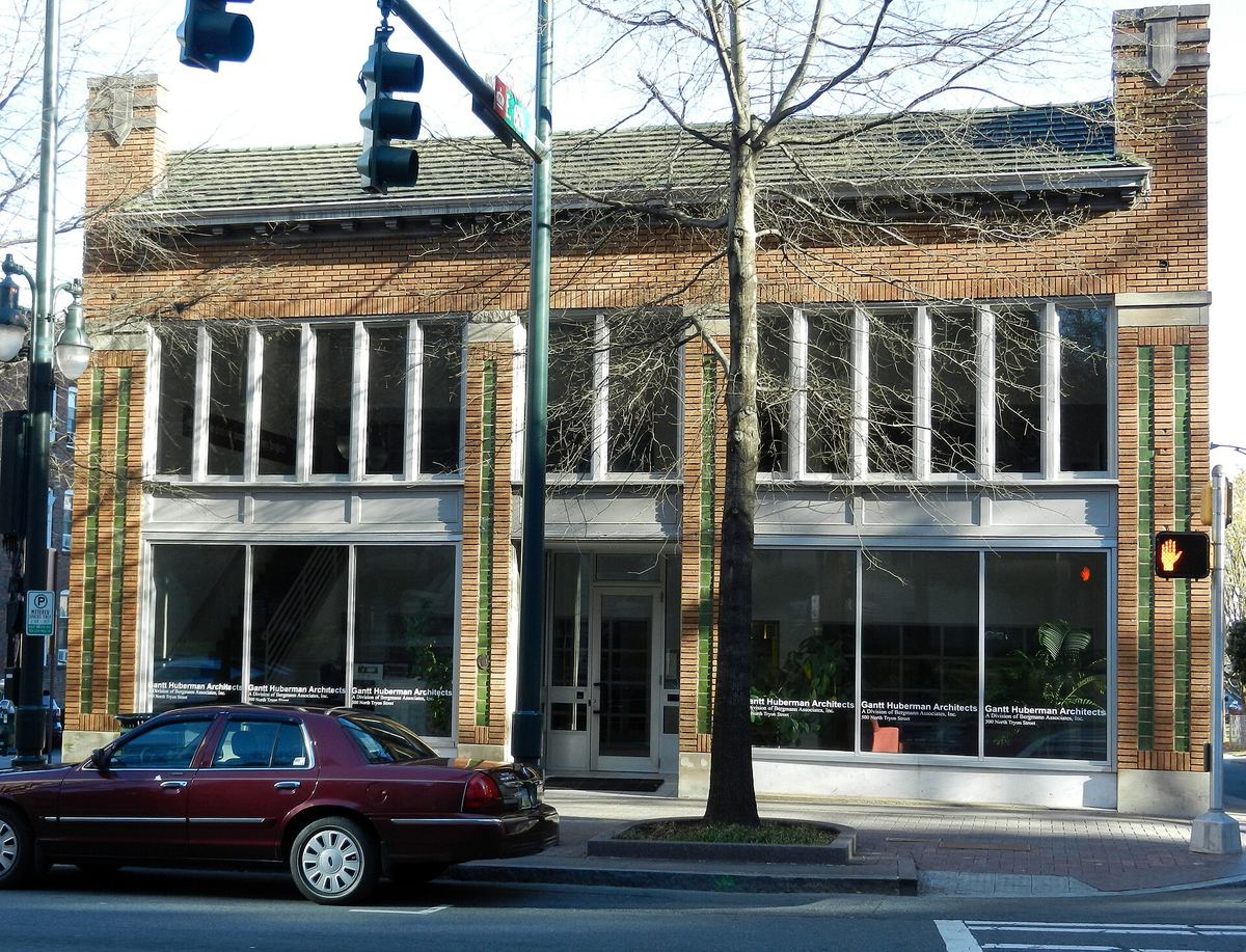 Two-storey commercial building on a street corner with a decorative green and cream tiled facade, large plate-glass shopfronts and a car parked at the kerb.