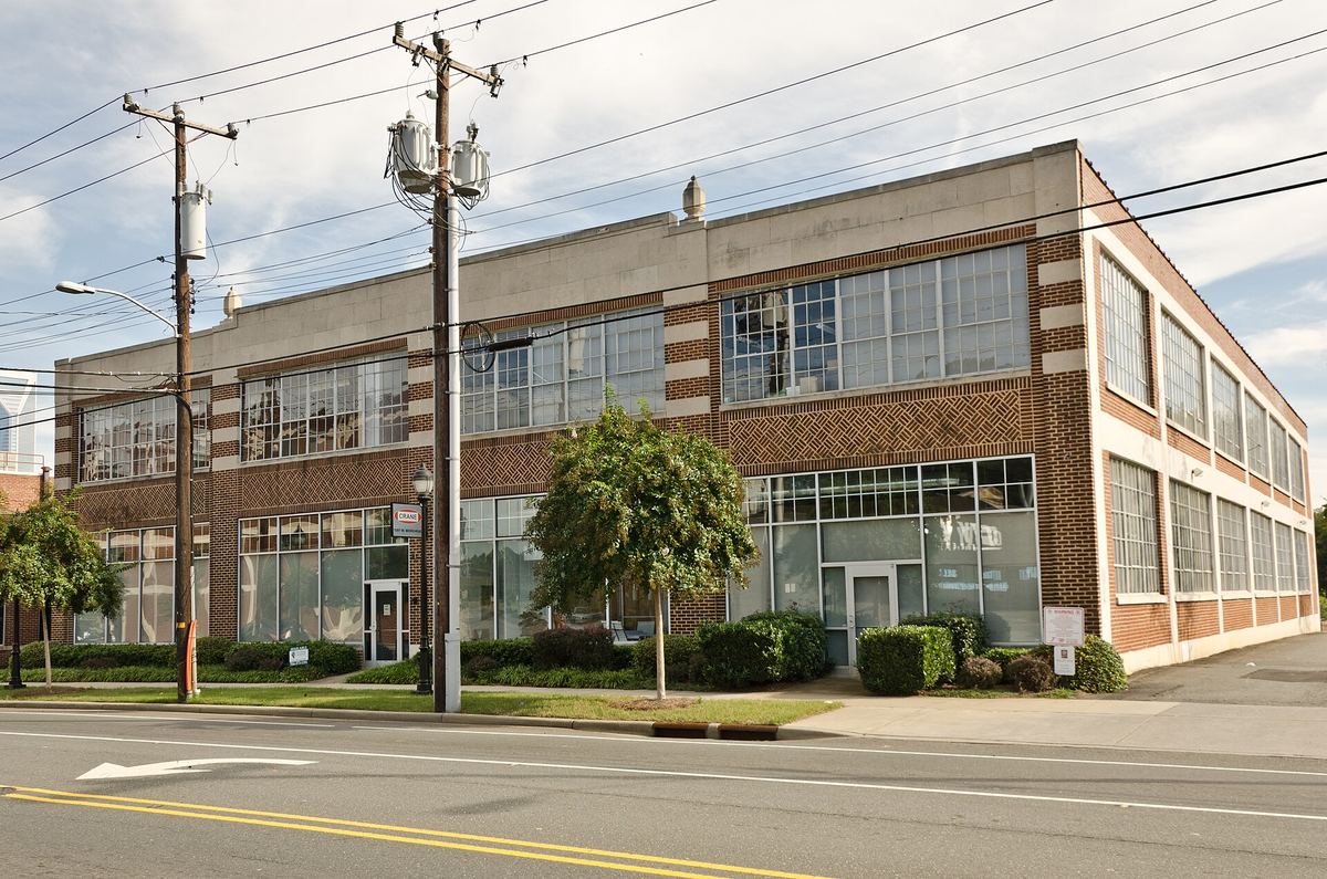 Long two-storey brick and glass industrial building on a corner, with continuous bands of steel-framed windows and overhead power lines.