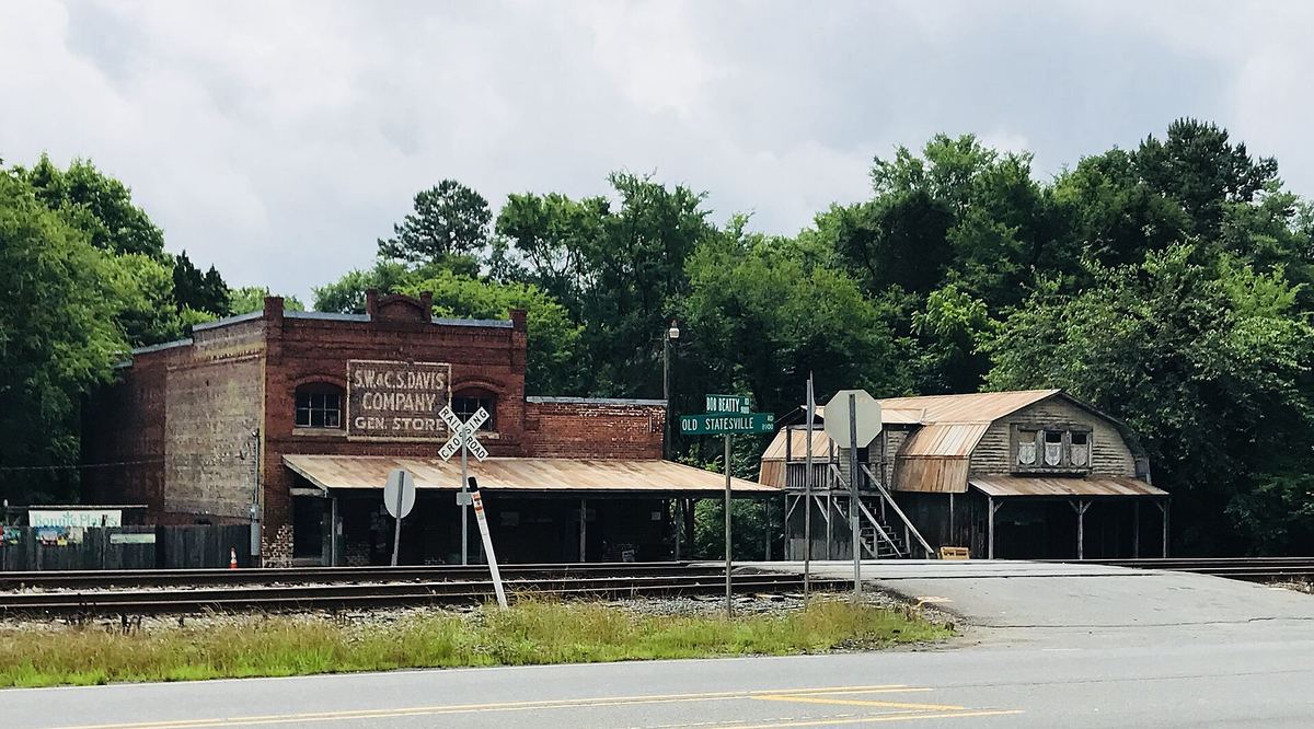 Small red brick store building beside a railway crossing, with a timber shed structure alongside and trees behind.