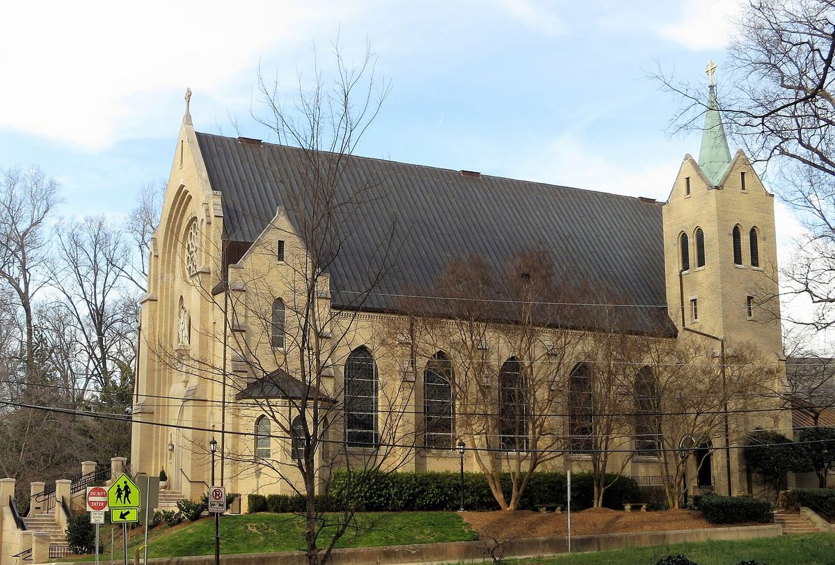 Large stone church with a steeply pitched dark roof, lancet windows and a tall square corner tower topped by a slender spire.