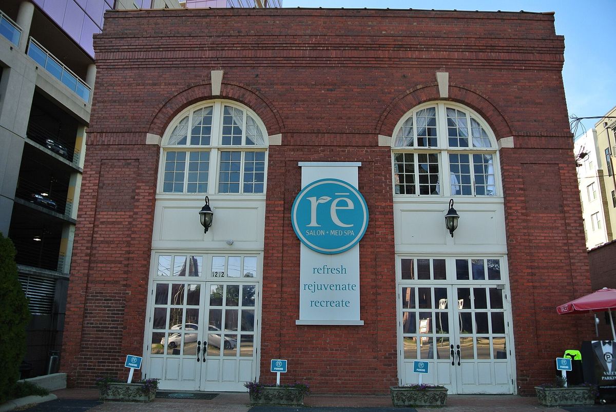 Red brick building with two tall arched openings filled with glazing, a circular blue sign on the brickwork between them and planters on the pavement.