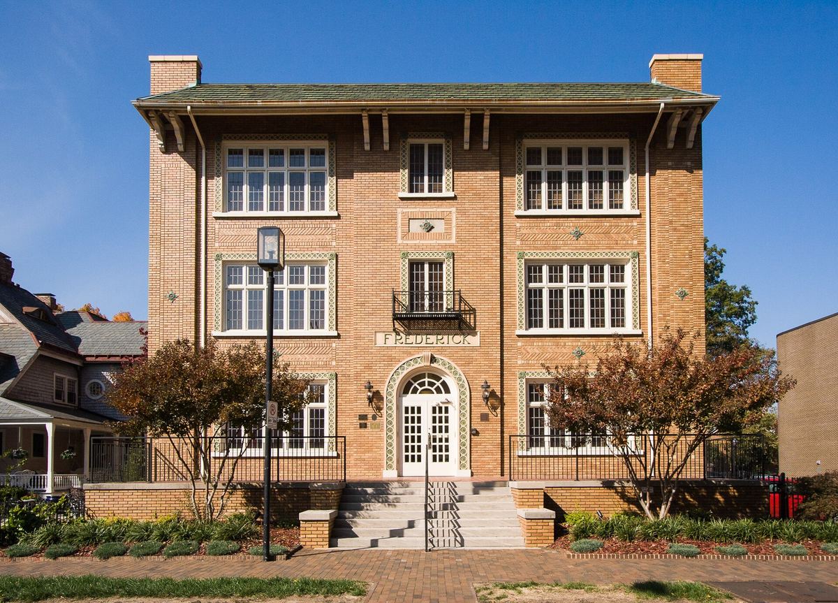Three-storey brick apartment building with stone banding, tall casement windows and an arched entrance reached by steps.