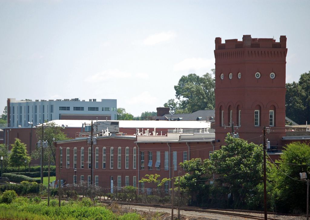 Red brick mill complex with a tall crenellated tower, seen across scrubland and a railway line.