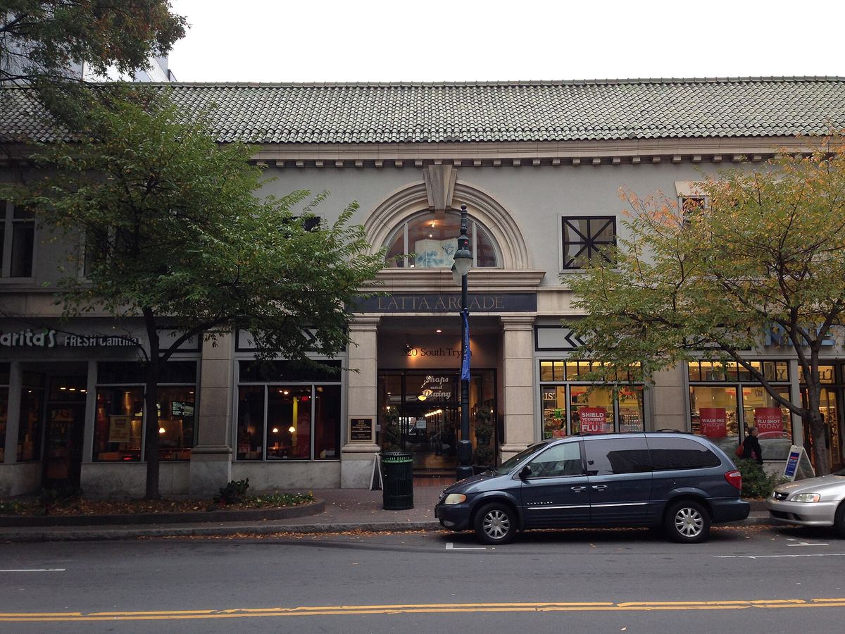 Street elevation of a two-storey commercial building with a tiled roof, arched central entrance and shopfronts, cars parked along the kerb.
