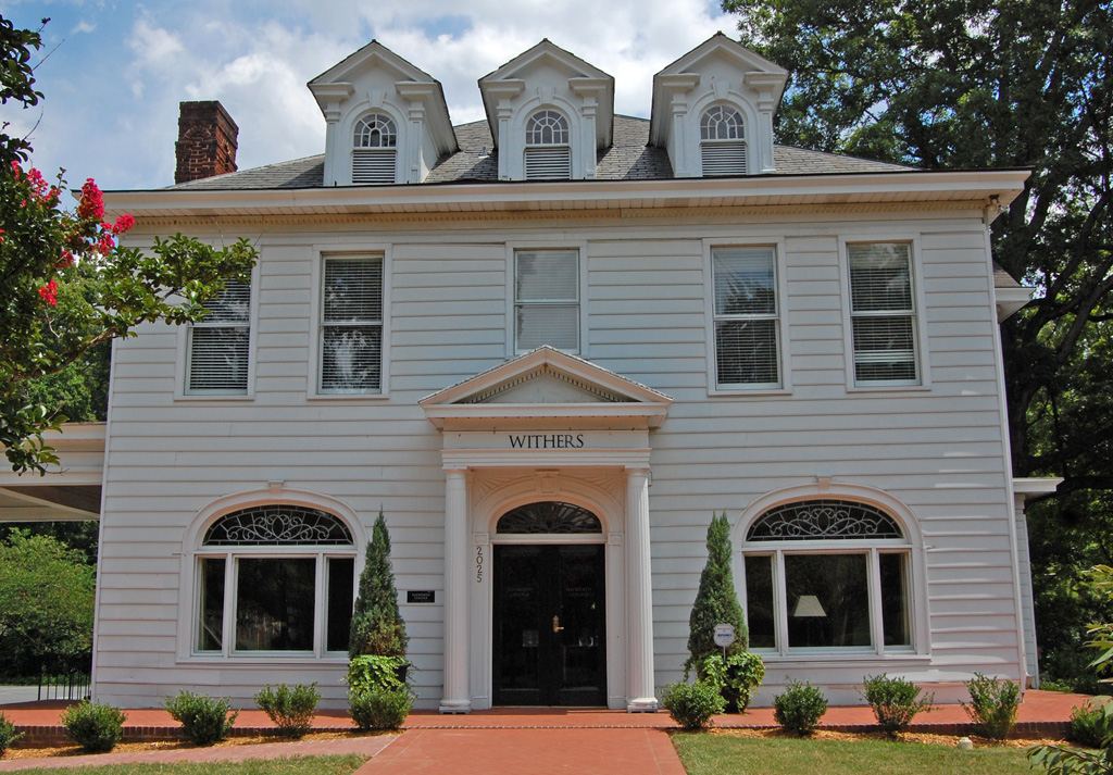 Two-storey white house with three arched dormer windows, an arched entrance surround and clipped conical shrubs either side of the door.