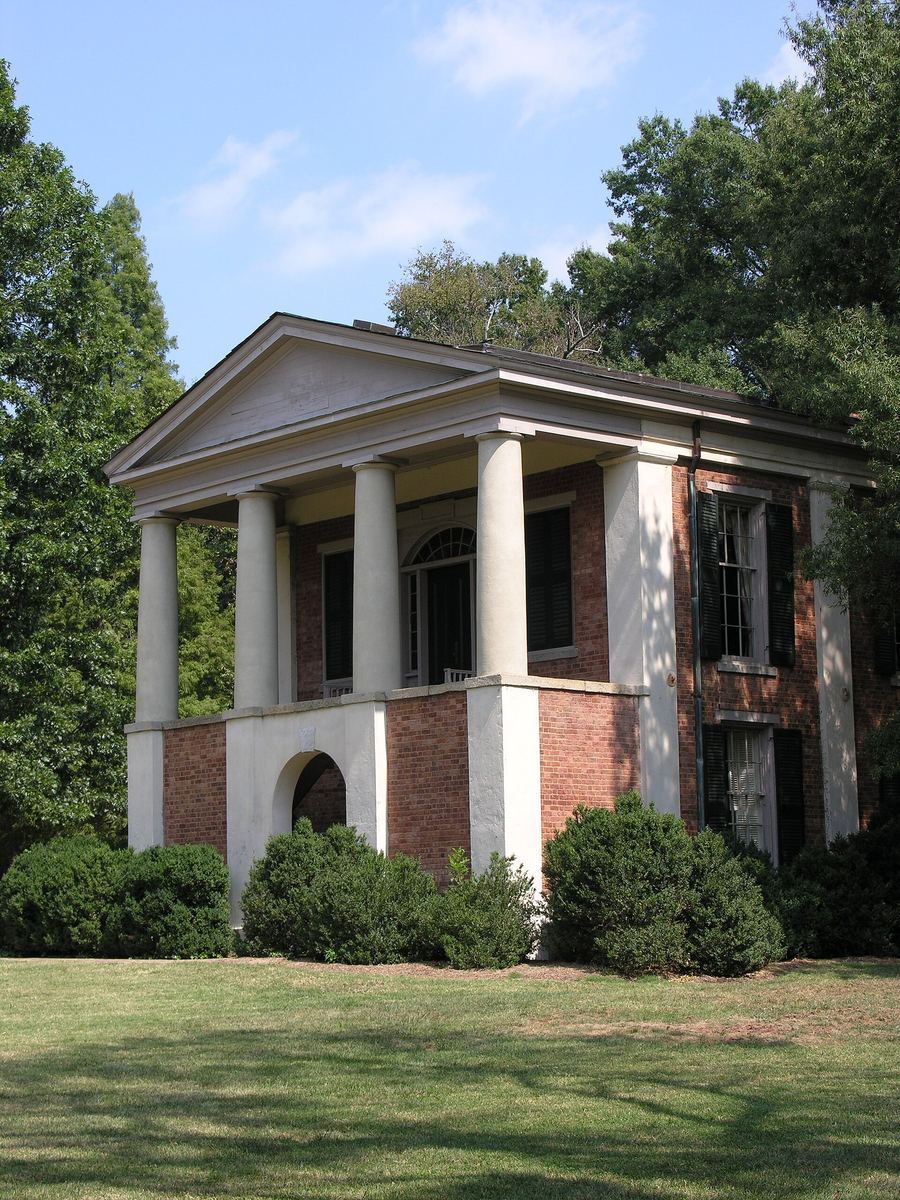 Small brick building with a white pedimented portico carried on four square columns, standing on a mown lawn.