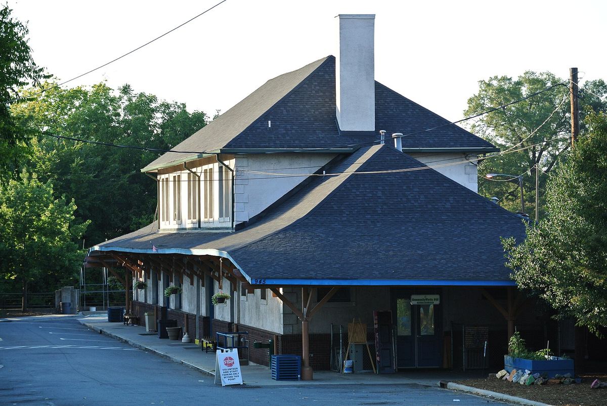 Single-storey railway station building with deep overhanging eaves, a blue slate roof and a canopy over the platform side, with tarmac in front.