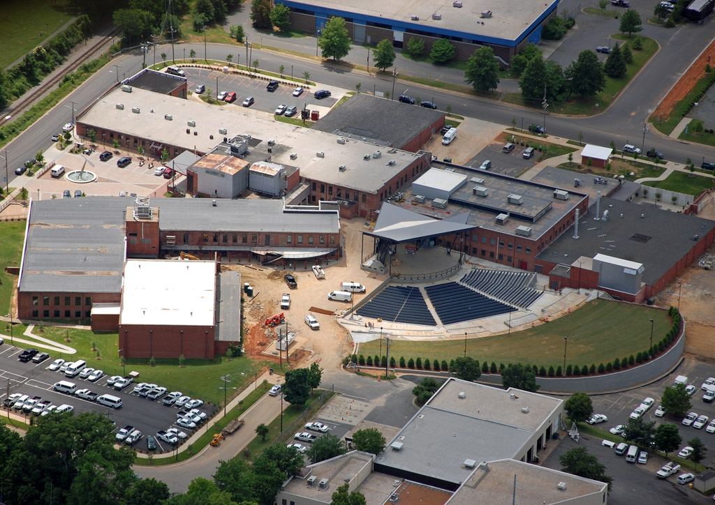 Aerial view of a large mill complex converted to a shopping and office development, with car parks, flat roofs and a curving landscaped area.