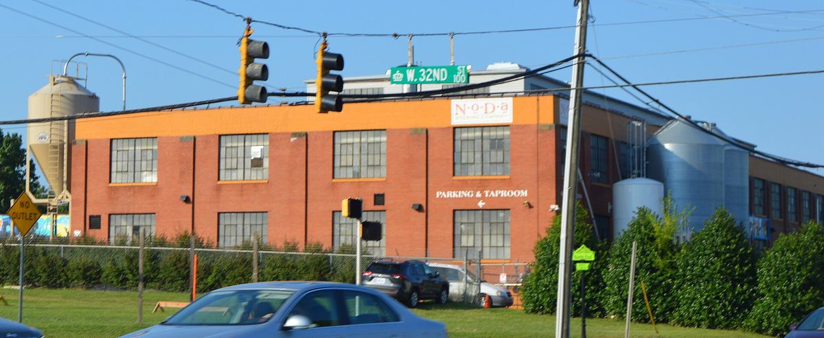 Two-storey orange-painted brick industrial building at a traffic-light junction, with silver silos and a blue-clad shed alongside.