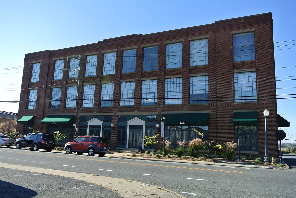 Three-storey red brick warehouse with regular windows, green awnings over the ground floor and cars parked along a wide road.