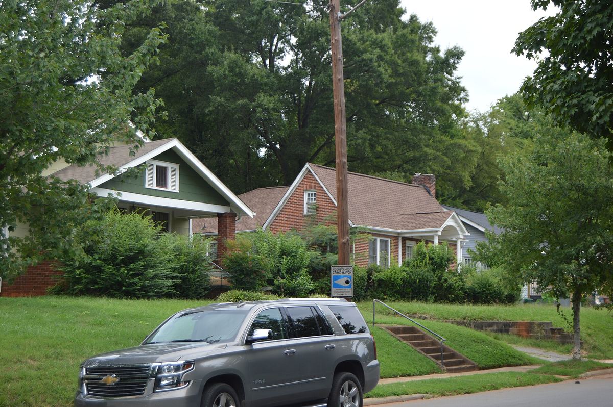 Single-storey brick and weatherboarded bungalows on a rising lawn beside a road, with a silver car parked at the kerb.