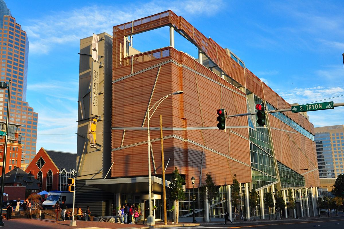 Angular modern building clad in bronze-coloured perforated metal panels, on a street corner with traffic lights and pedestrians.