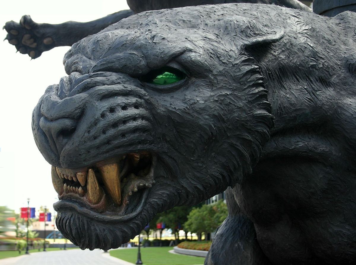 Close view of a large bronze sculpture of a snarling panther with green eyes, mounted outdoors.