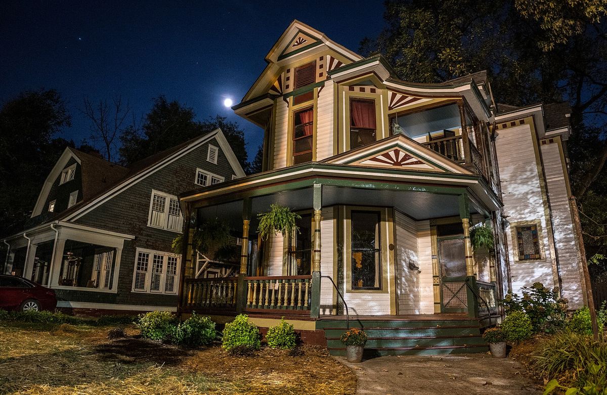 Ornate two-storey Queen Anne house photographed at dusk with warm interior lighting, decorative porch and gables.