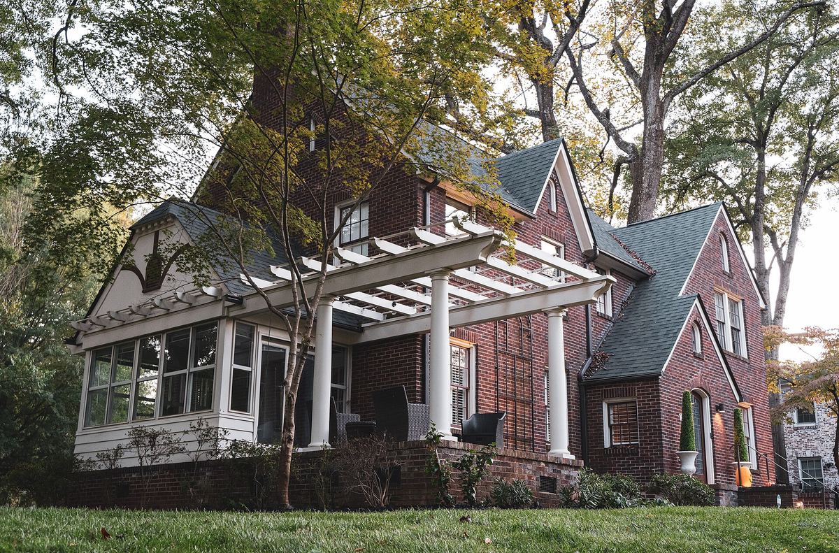 Row of single-storey bungalows with pergolas and porches, set behind mature trees in autumn.