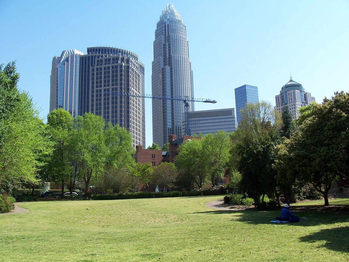 A city skyline of glass towers seen across an open park lawn fringed with trees.