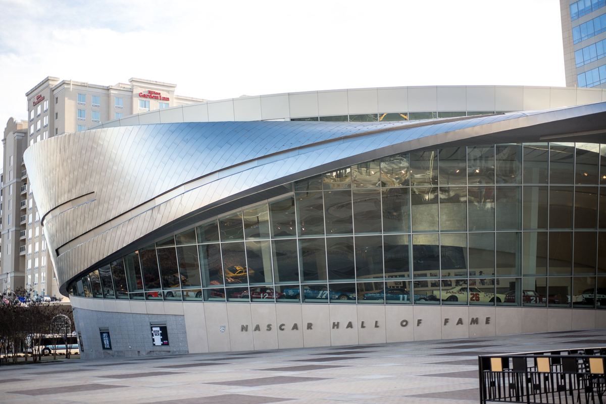 Curved silver façade and glass windows of the NASCAR Hall of Fame, with its name above the entrance.